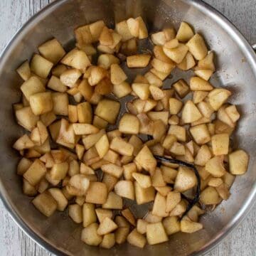 Chopped apple coated in ground cinnamon in a frying pan.