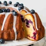 Blueberry pound cake on a white cake stand with a slice cut and pulled out.