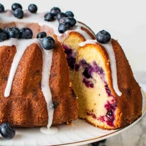 Blueberry pound cake on a white cake stand with a slice cut and pulled out.