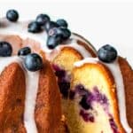 Blueberry pound cake on a white cake stand with a slice cut and pulled out.