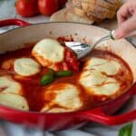 Chicken Pizzaiola in a red skillet with one piece being lifted out with a spoon.