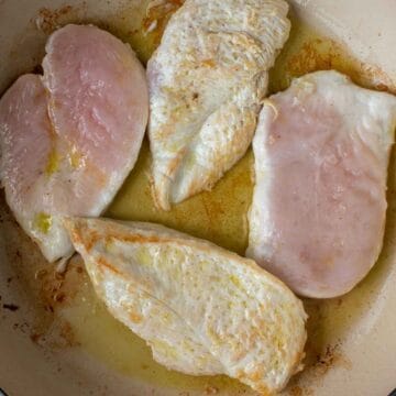 Four chicken cutlets being seared in a pan.