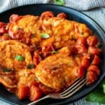 Chicken pomodoro with cherry tomatoes and fresh basil scattered around on a black plate.