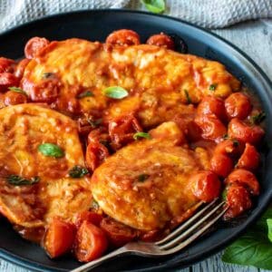 Chicken pomodoro with cherry tomatoes and fresh basil scattered around on a black plate.