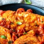 Chicken pomodoro with cherry tomatoes and fresh basil scattered around on a black plate.