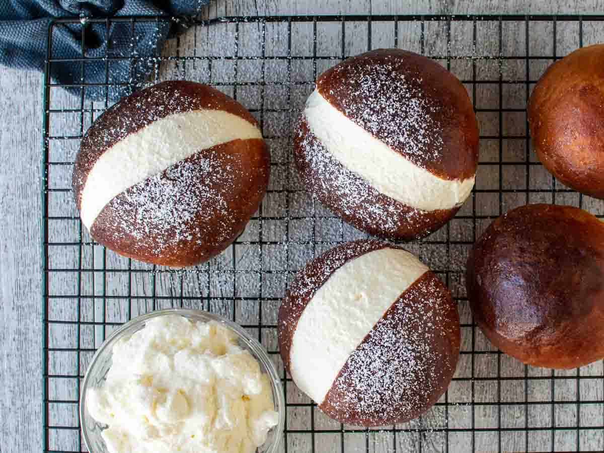 Overhead view of golden brown cream buns dusted with powdered sugar on a black wire rack.