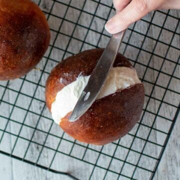 A knife leveling off cream in a brown bun.