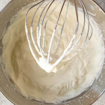 Whipped cream in a steel bowl with whisk attachment held above the bowl.