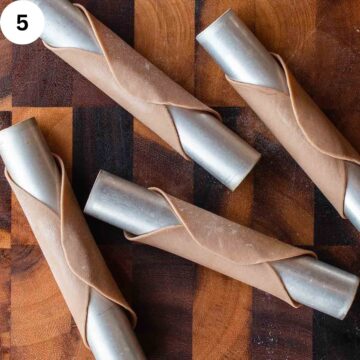 Brown pasta dough rolled around stainless steel tubes.