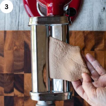 Dark pasta being rolled through KitchenAid pasta roller.