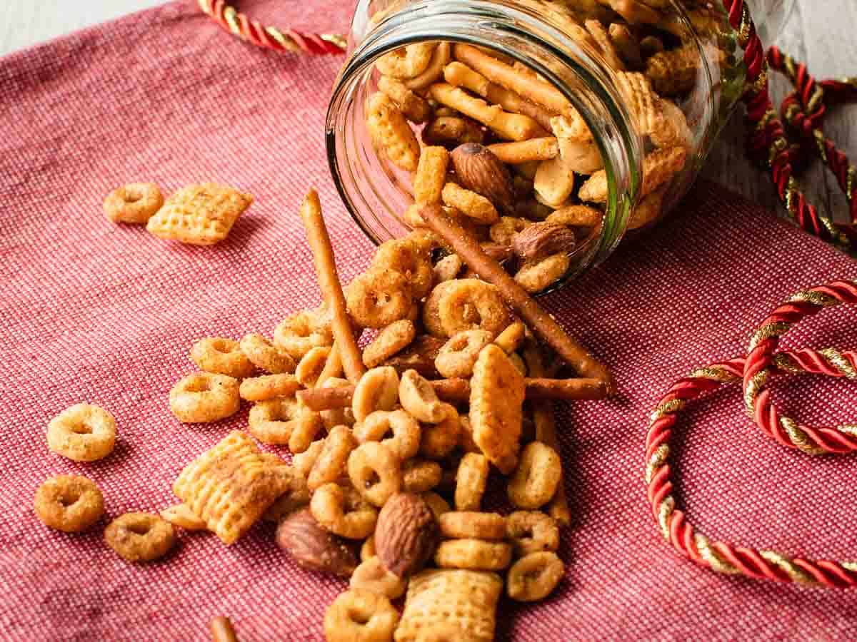 Mixture of cereals, nuts and pretzels spilling out of overturned jar.