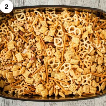 Mixed varieties of cereal, nuts and pretzels combined in a baking pan.