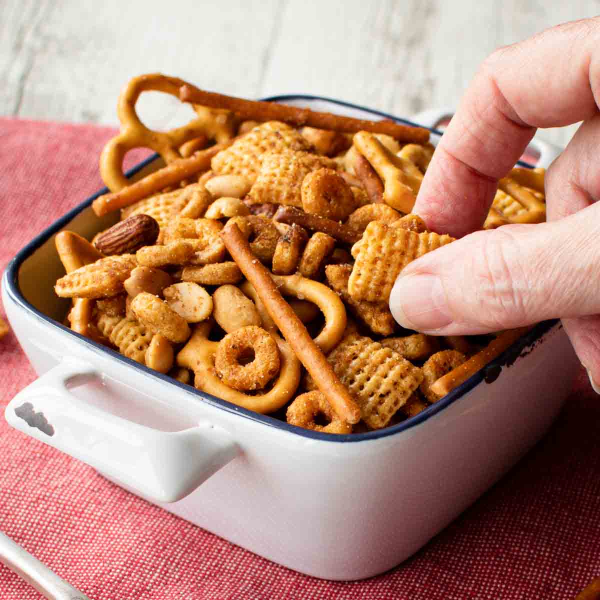 Nuts and Bolts in a white square ceramic bowl with fingers picking up some.
