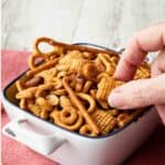Nuts and Bolts in a white square ceramic bowl with fingers picking up some.