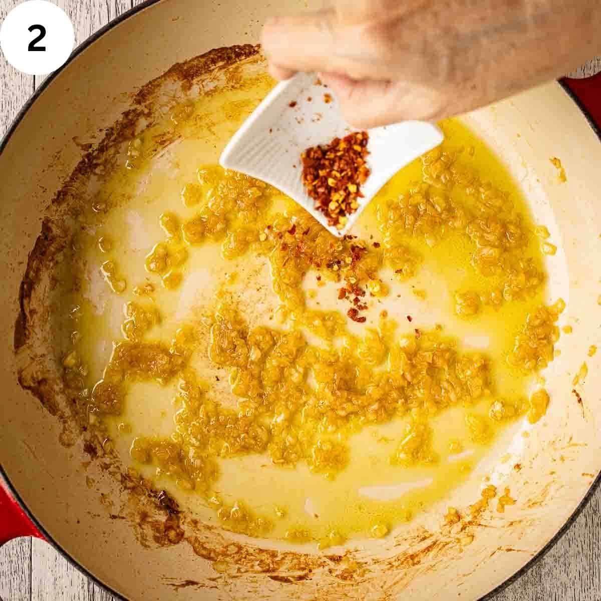 Adding red pepper flakes to fried onion in a pan.