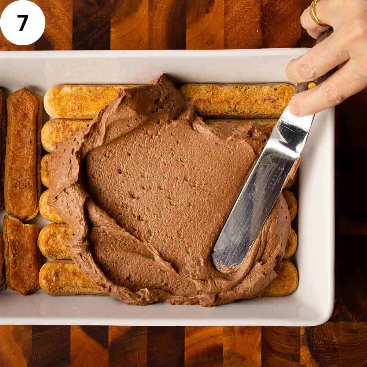 Chocolate cream being spread over savoiardi cookies.
