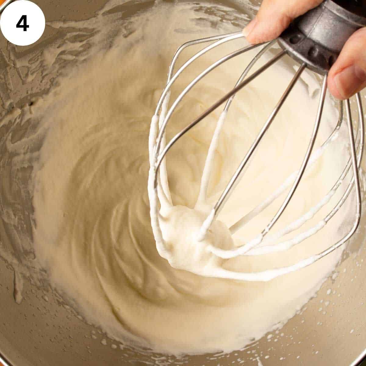 Whipped cream in a stainless steel bowl with wire whisk.