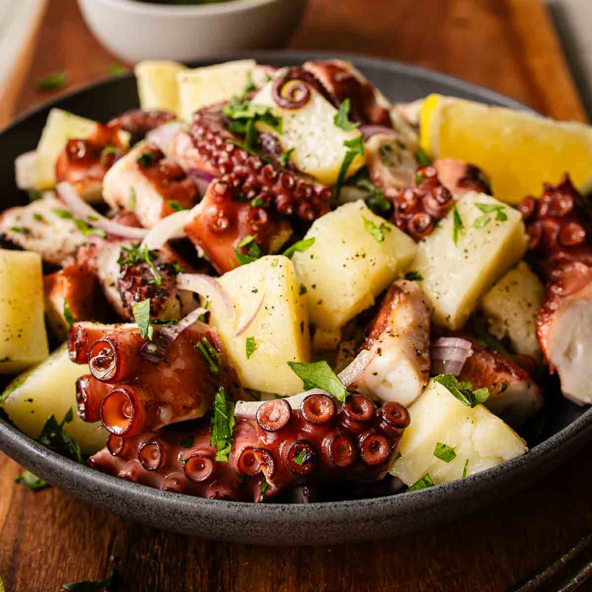Octopus salad in a bowl on a wooden board.