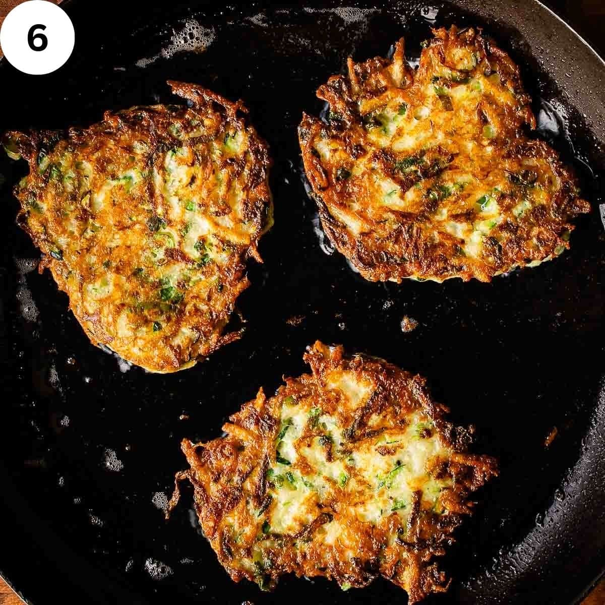 Three browned zucchini pancakes in a black skillet.