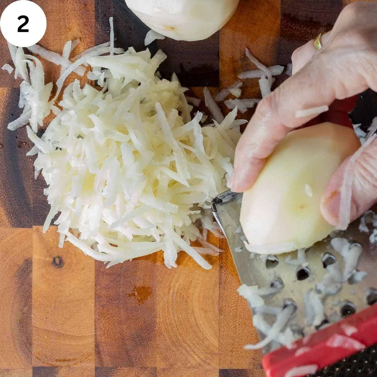 Peeled potato being shredded on a coarse grater.