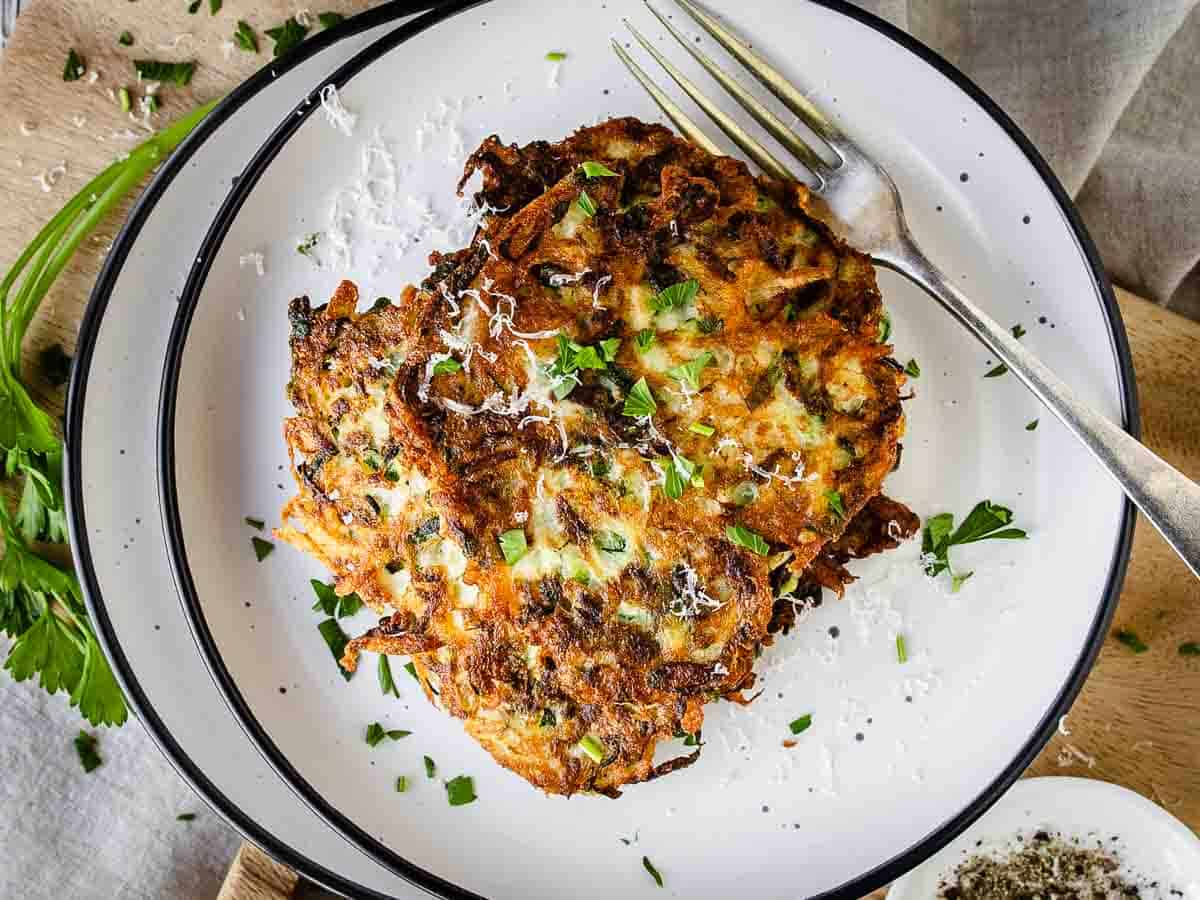 Overhead view of zucchini and potato fritters stacked on a plate.