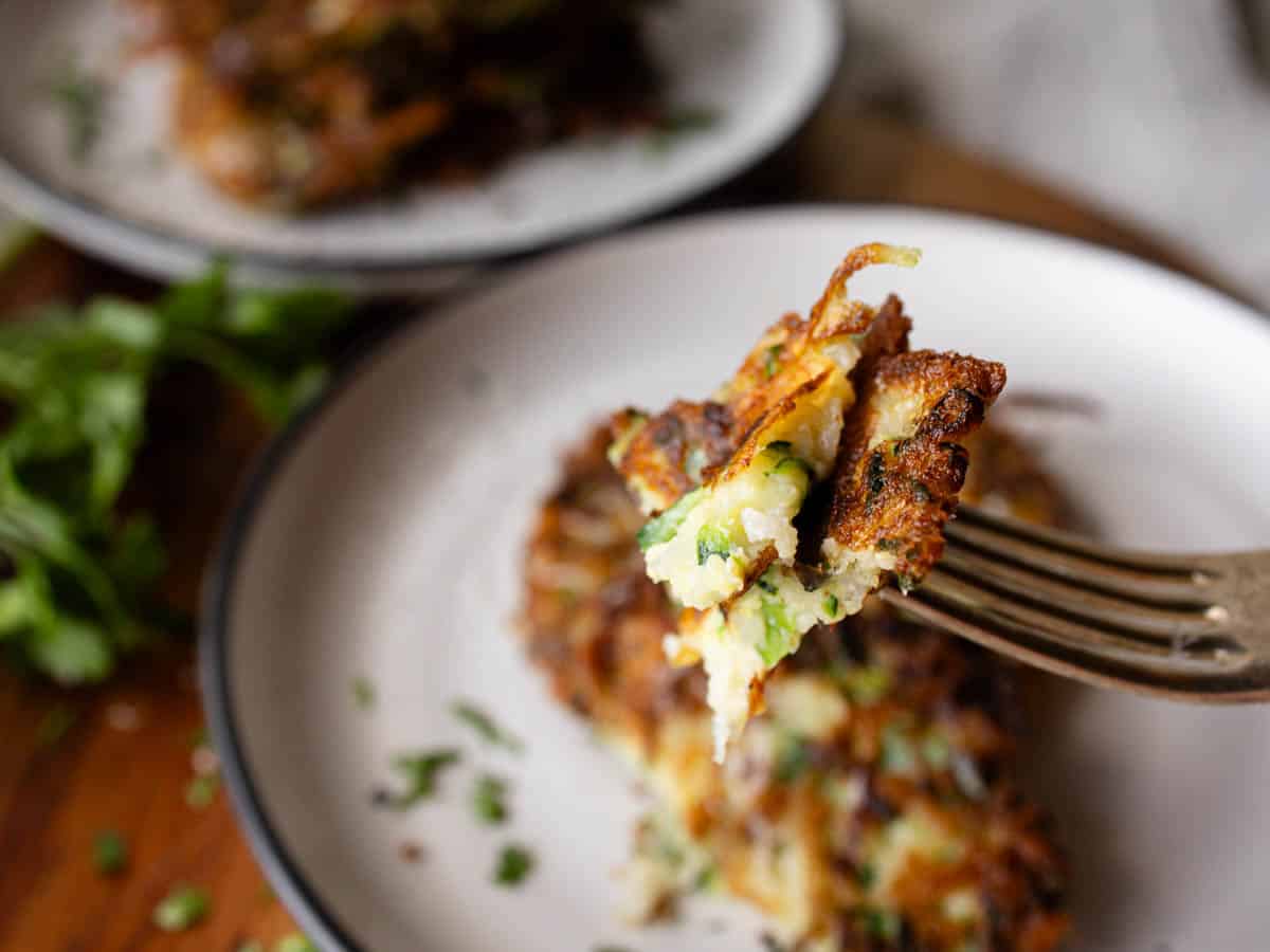 A closeup of a piece of zucchini potato fritter on a fork.