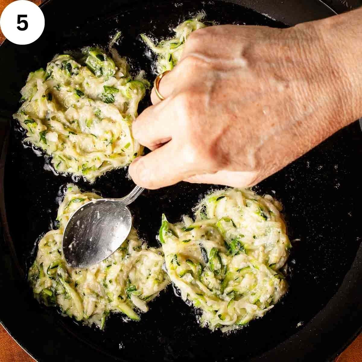 Zucchini fritters being fried in a pan.