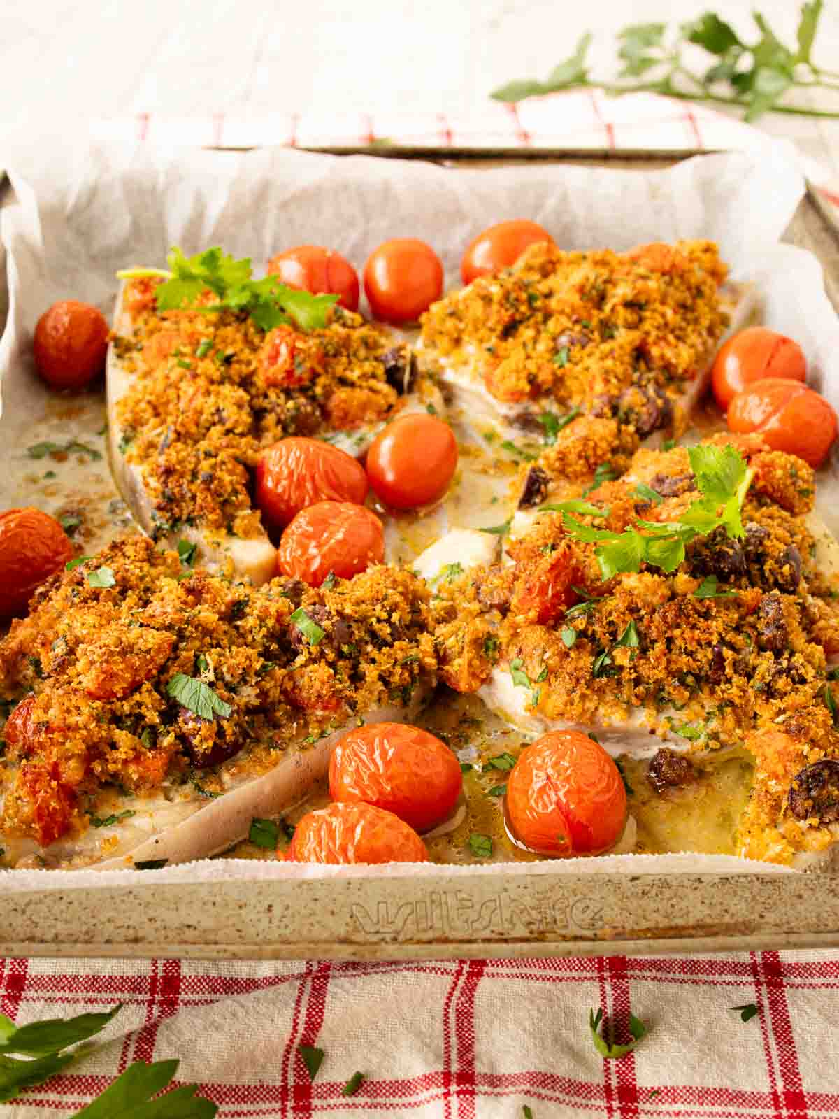 Baked Swordfish with a gratin topping surrounded by baked cherry tomatoes.
