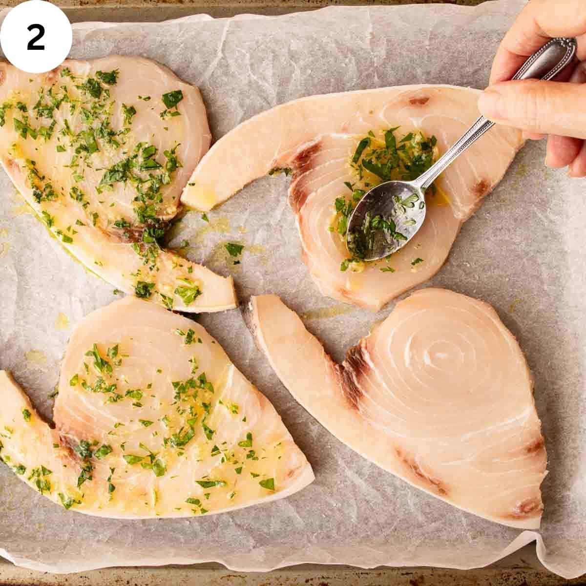 Using a spoon to drizzle herb dressing on swordfish steaks.