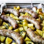 Baked Italian sausages and potatoes in a baking dish.
