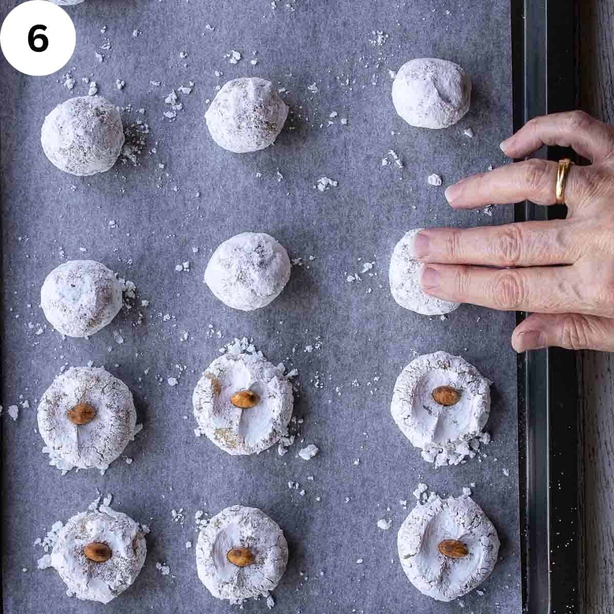 Fingers pressing on powdered sugar coated dough balls.