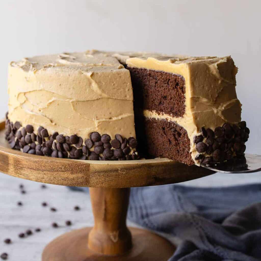 Chocolate and peanut butter cake on a wooden cake stand with a slice cut.