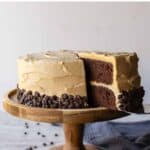 Chocolate and peanut butter cake on a wooden cake stand with a slice cut.