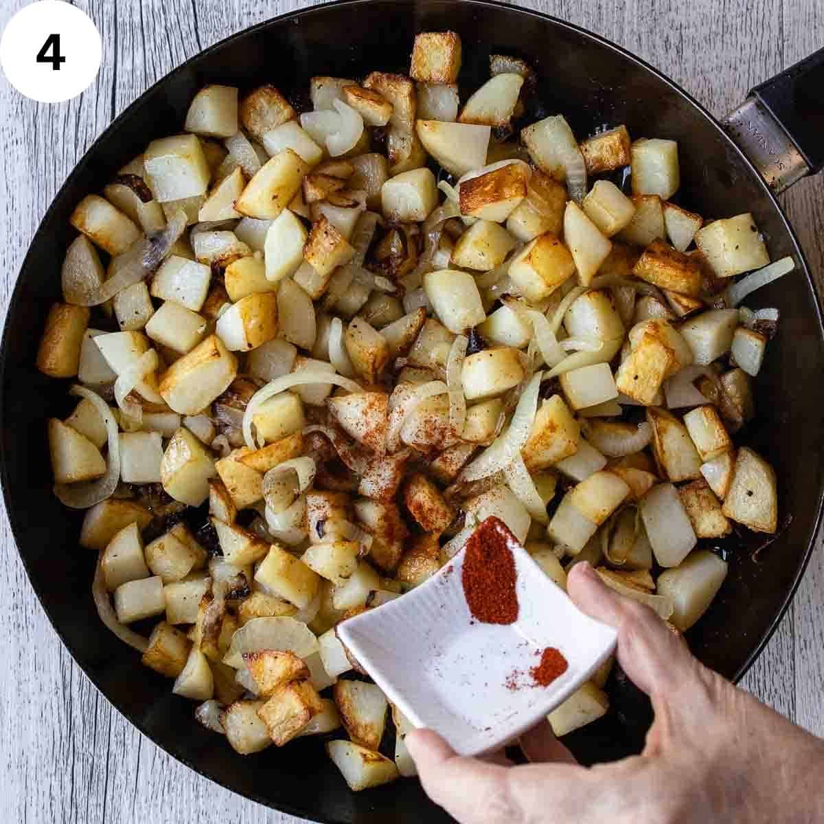 Sprinkling paprika into fried cubed potatoes.