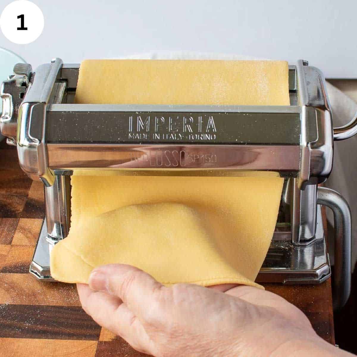 Pasta dough being rolled through a hand cranked pasta machine.