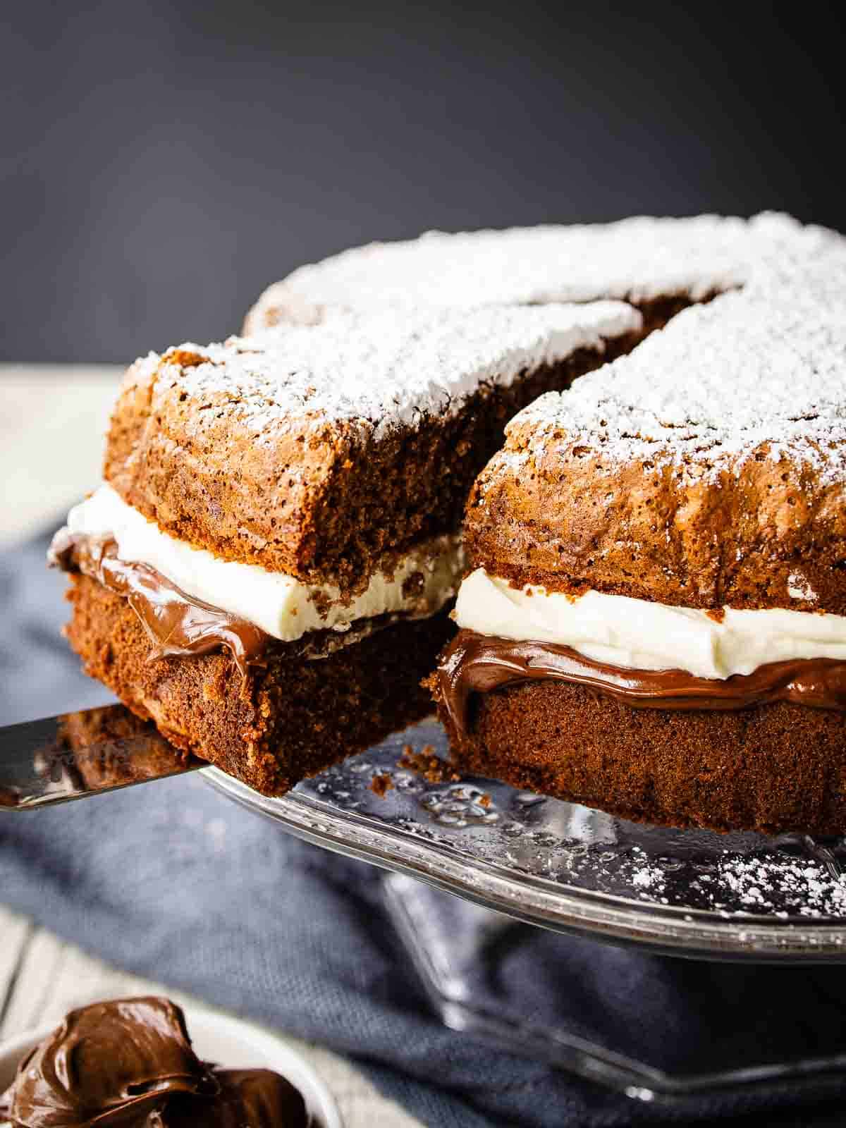 A two layered Nutella Cake filled with gooey chocolate and cream with a slice cut.
