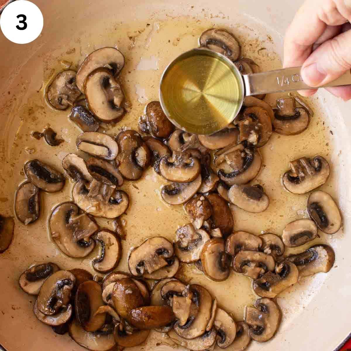 White wine being poured into a skillet of cooked, sliced mushrooms.