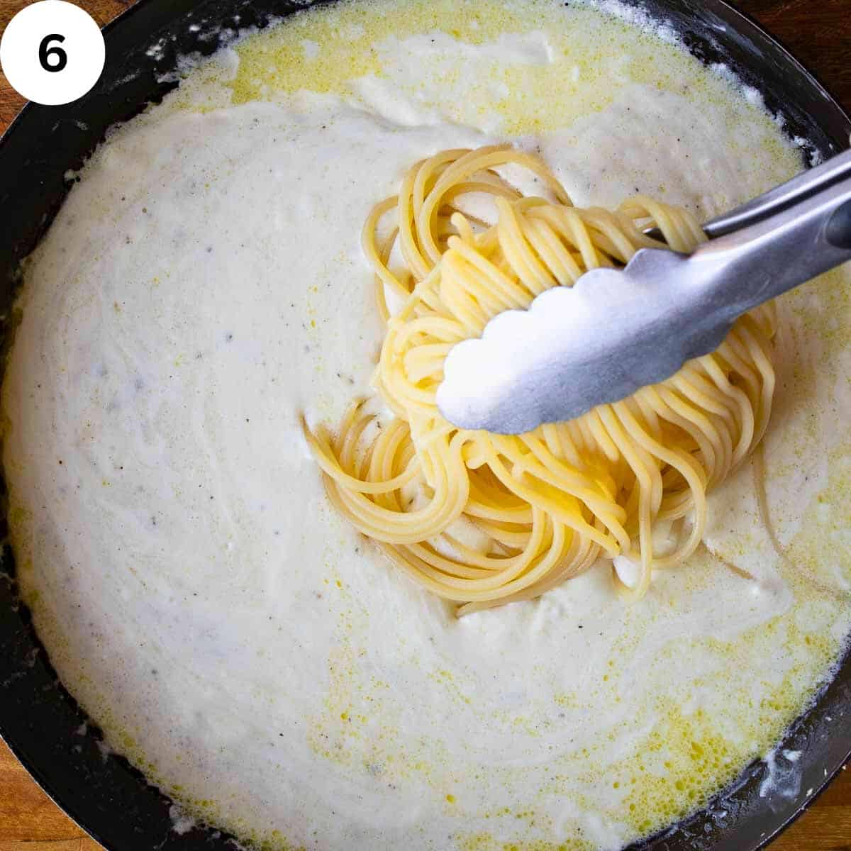 Cooked spaghetti being added to cream cheese sauce.