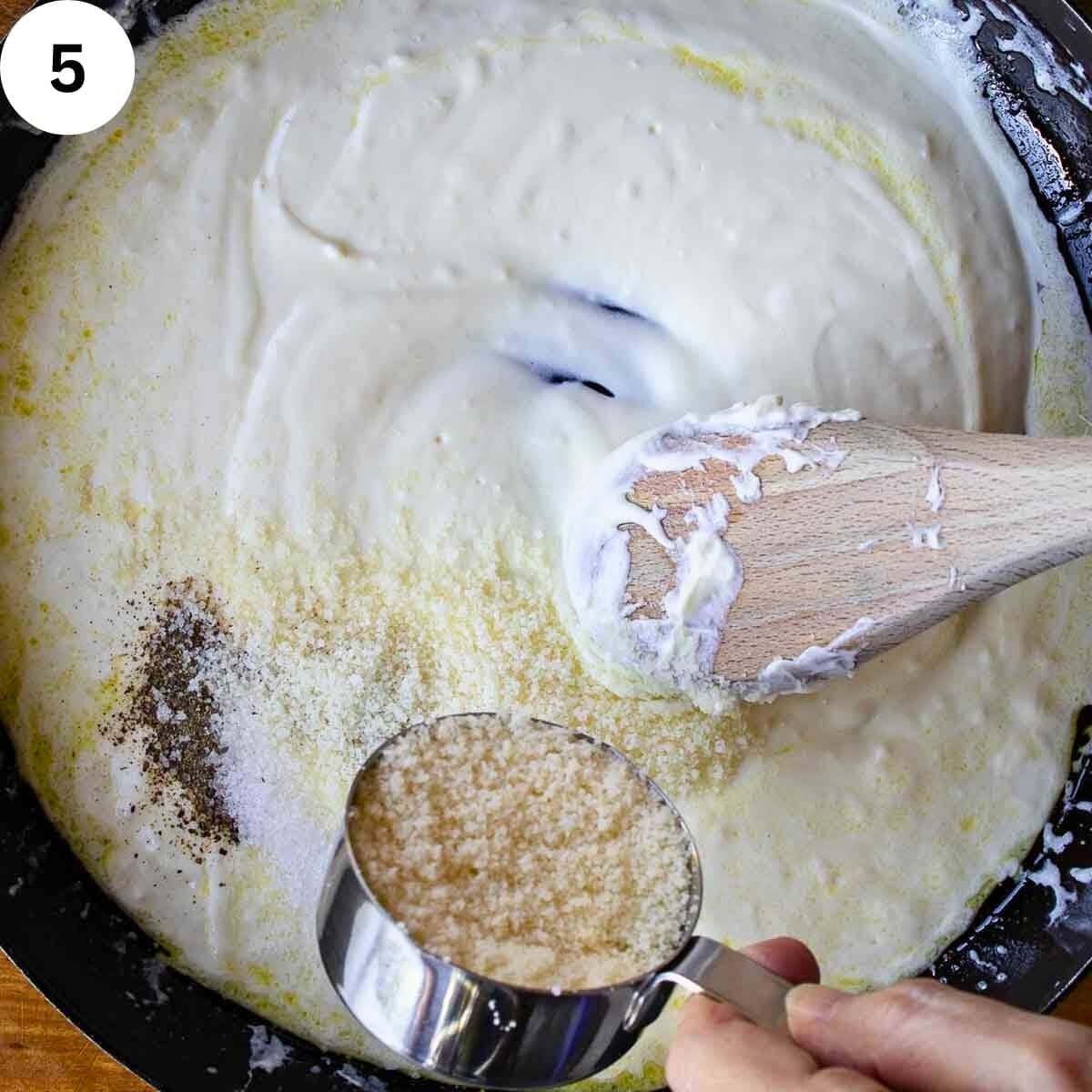 Freshly grated Parmesan cheese being added to cream sauce in a skillet.