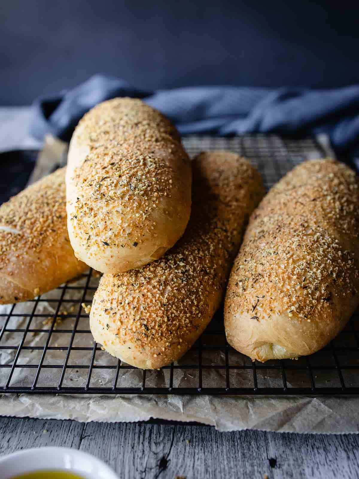 Italian cheese and herb bread loaves piled up on a wire rack.