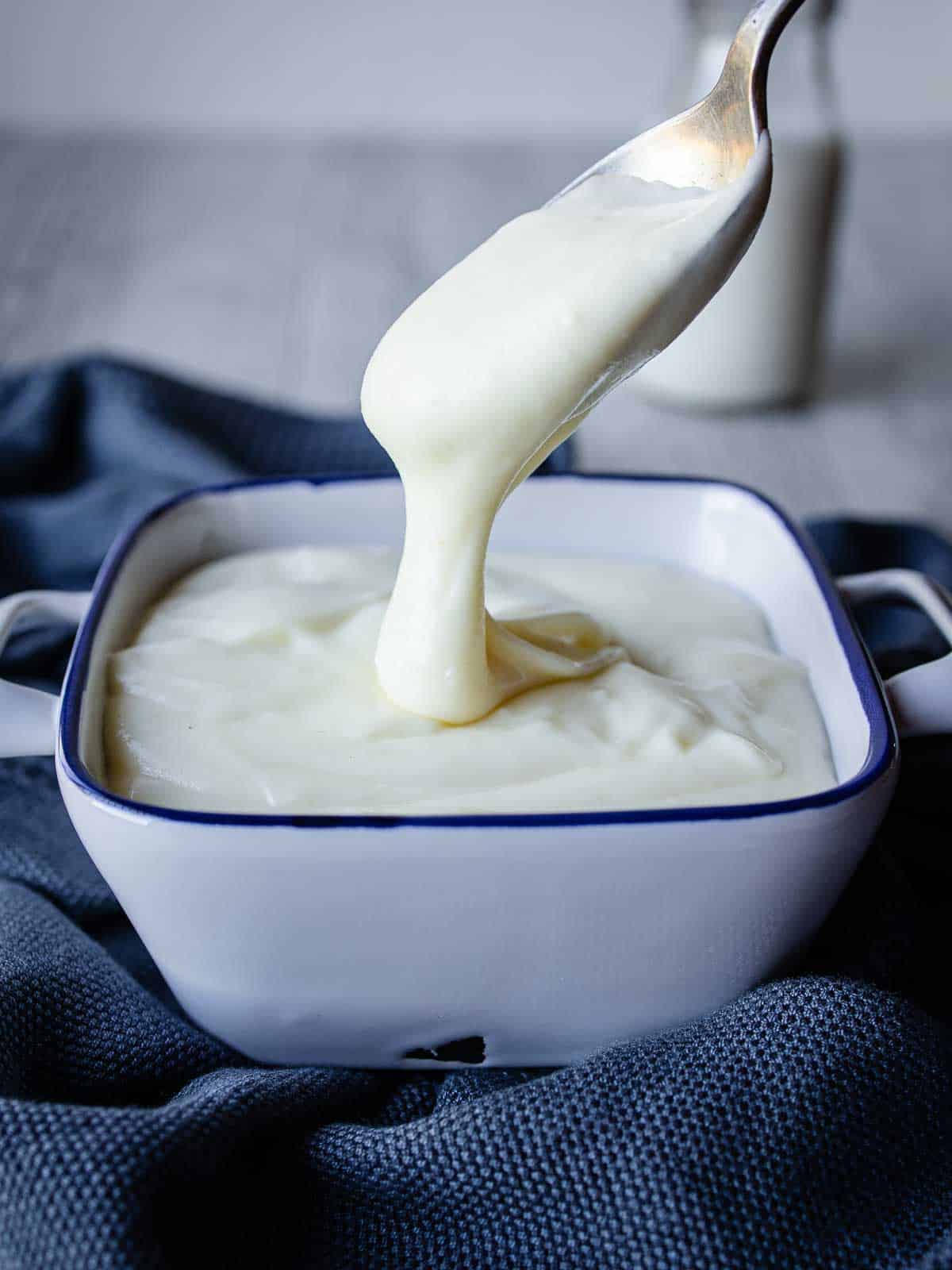 Besciamella sauce pouring off a spoon and into a bowl.