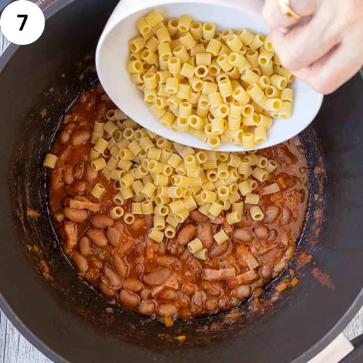 Pasta being added to a cooked mixture of borlotti beans and vegetables.