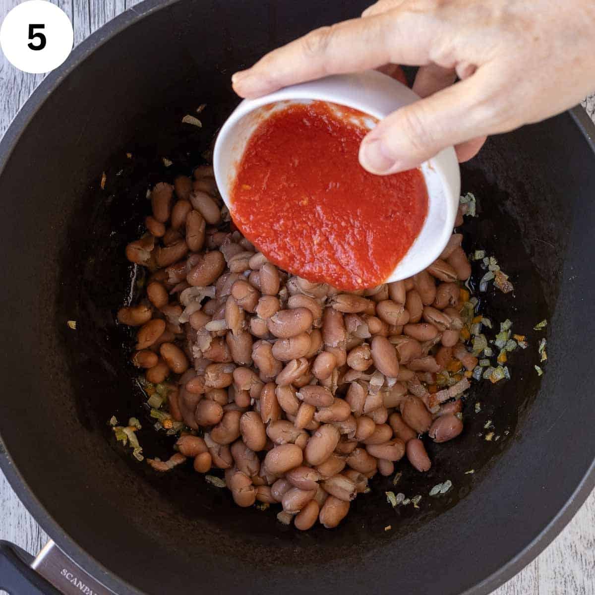 Tomato sauce being added to a saucepan of beans.