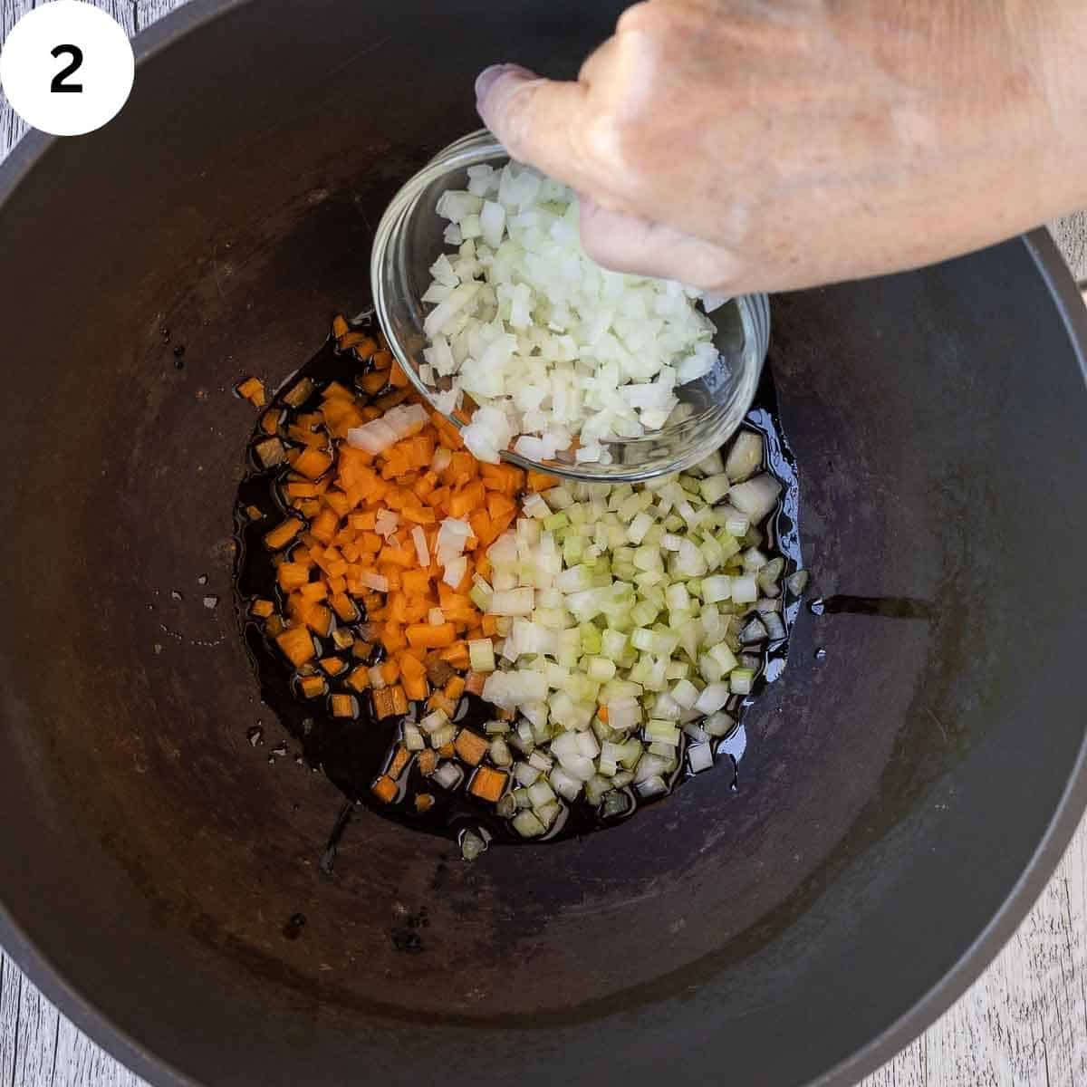 Finely chopped onion being added to a saucepan with chopped carrot and celery.
