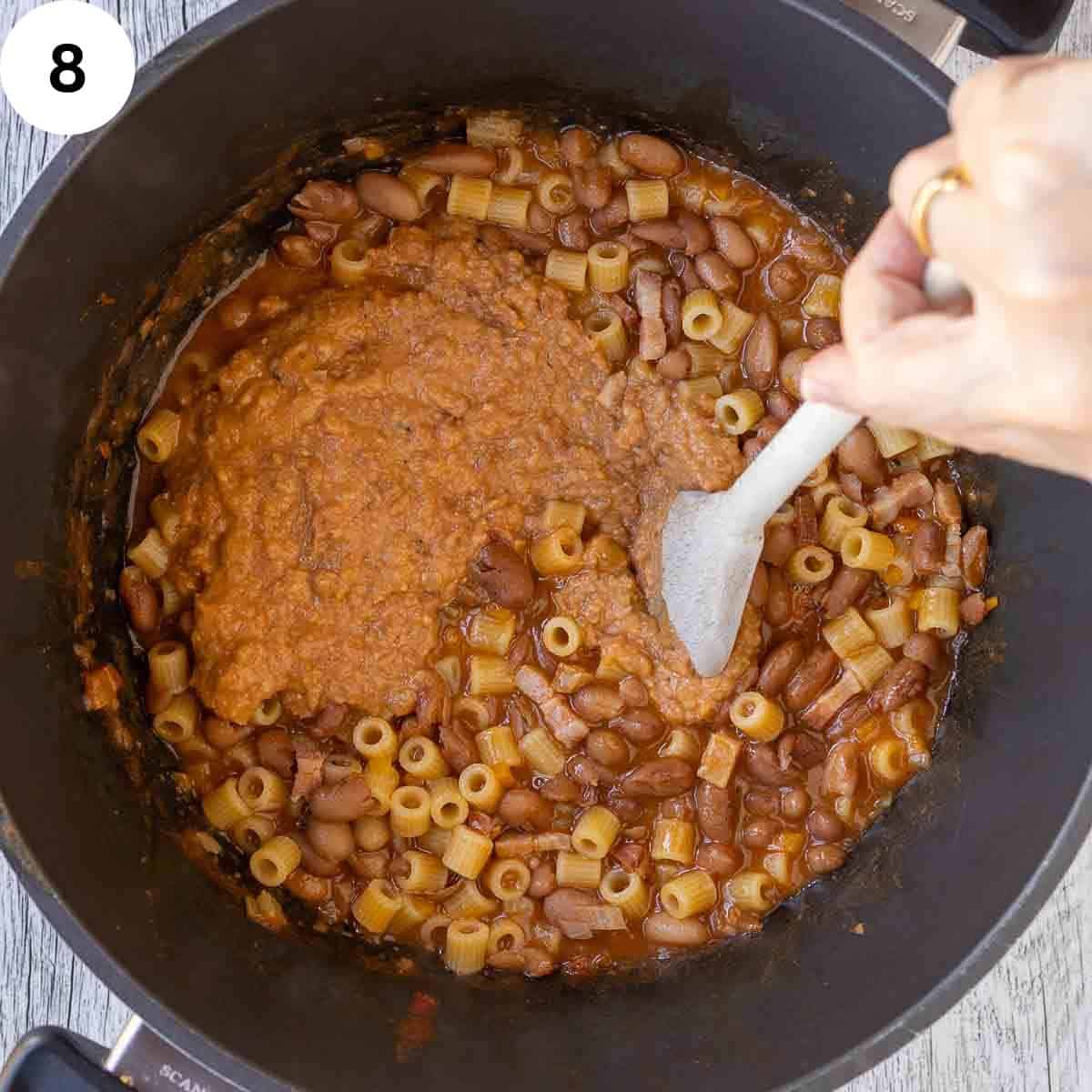Creamy mixture being stirred into cooked borlotti beans.