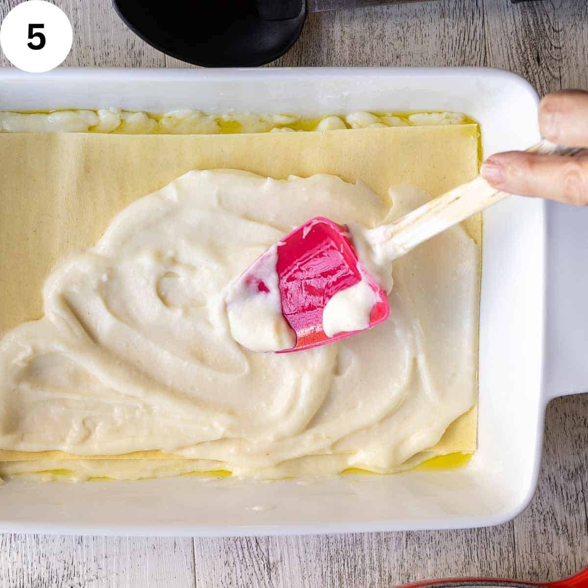 Spreading white sauce on lasagna noodle in a lasagna pan.
