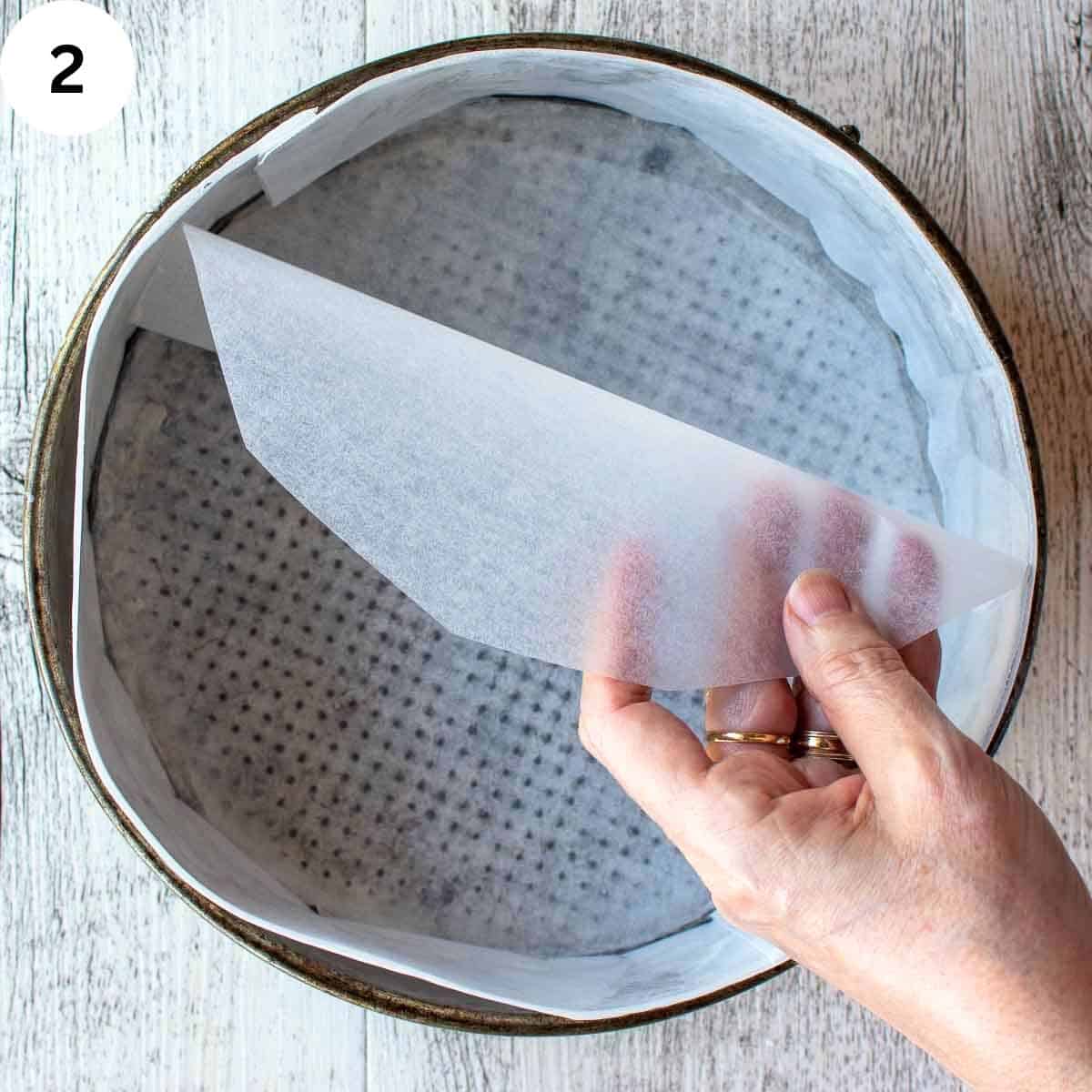 A round sheet of parchment being place into a round cake pan to line the bottom.