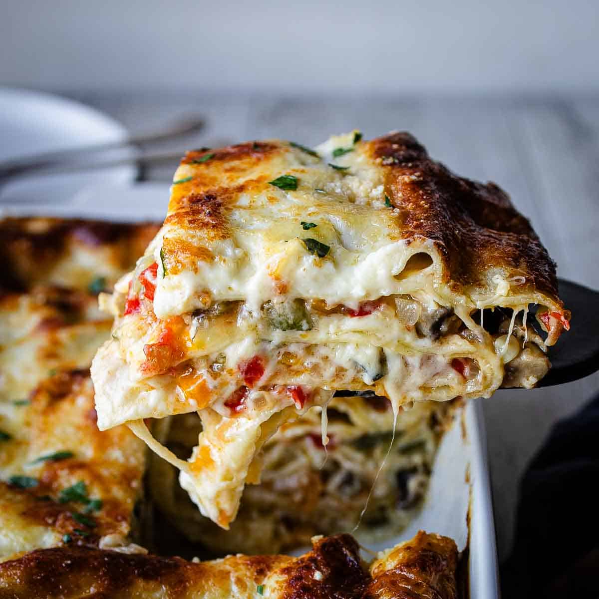 A slice of vegetable lasagna with white sauce being lifted out of a baking dish.