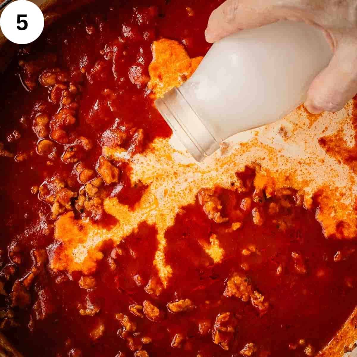 Pouring cream into tomato pasta sauce.