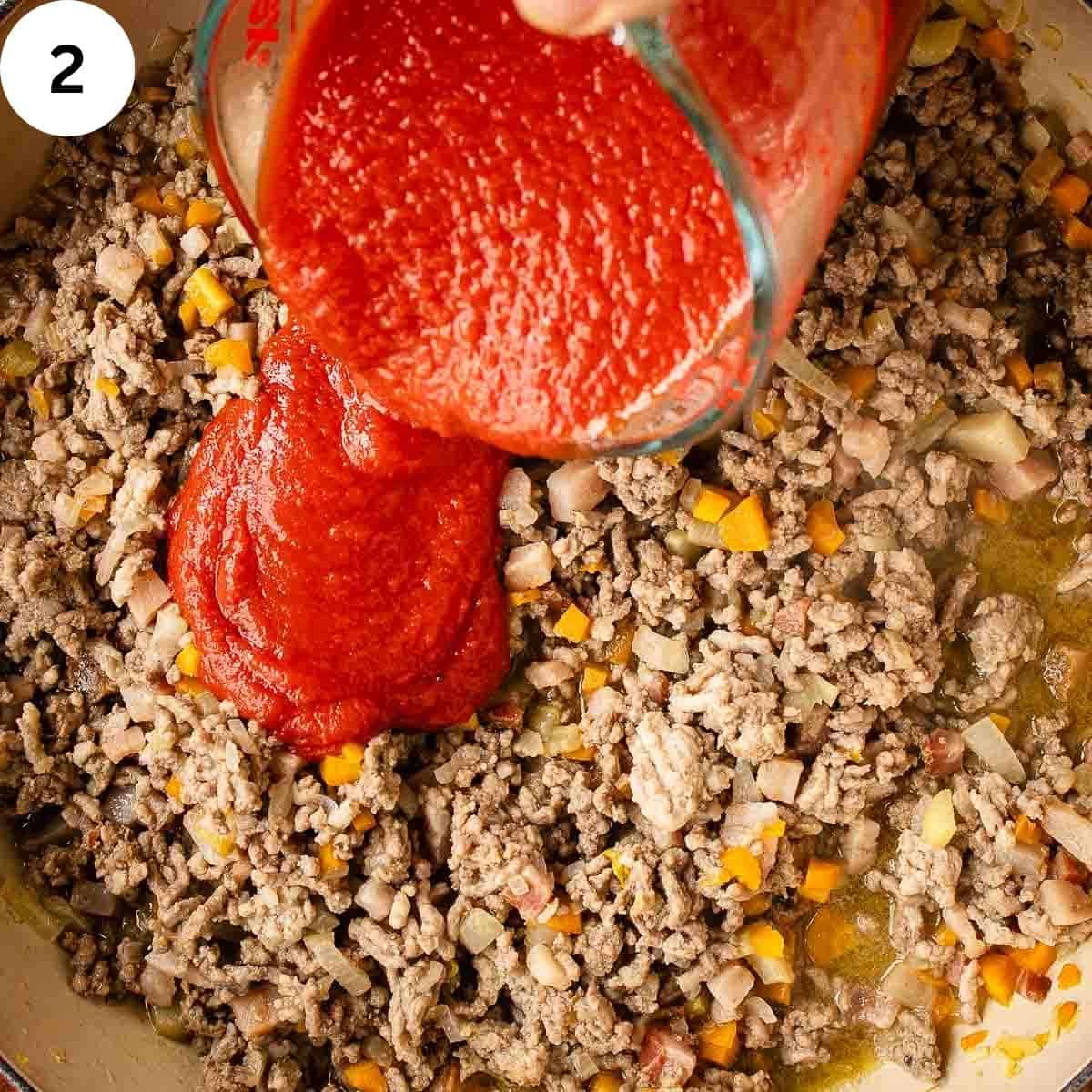Adding tomato sauce to browned, ground meat.